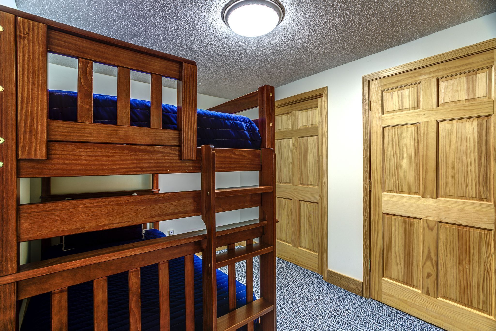 Una cama individual con estructura de madera y ropa de cama azul, una puerta de madera y piso alfombrado.