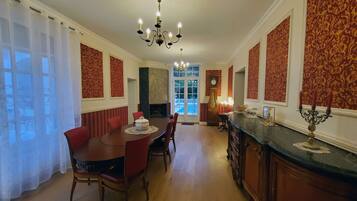 A dining room with a wooden table and red chairs, a chandelier, and a clock on the wall.