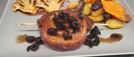 Un plato con un pincho de carne, patatas asadas y una guarnición que parece una preparación de verduras.