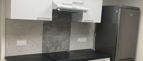 A modern kitchen with white cabinets, a black countertop, a built-in oven, a stainless steel refrigerator, and a skylight above.