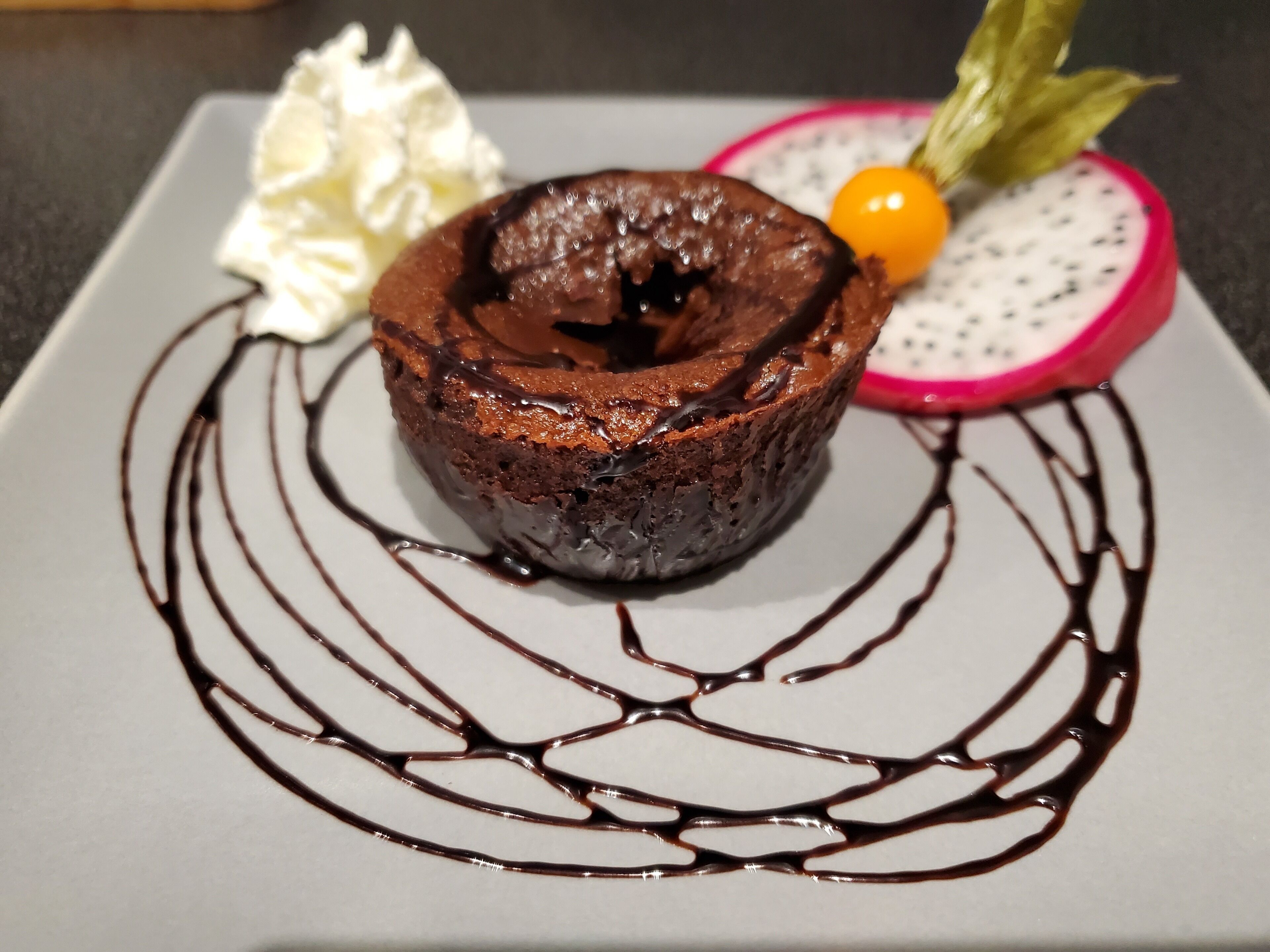 A dessert with chocolate lava cake, whipped cream, and a dragon fruit slice on a plate.