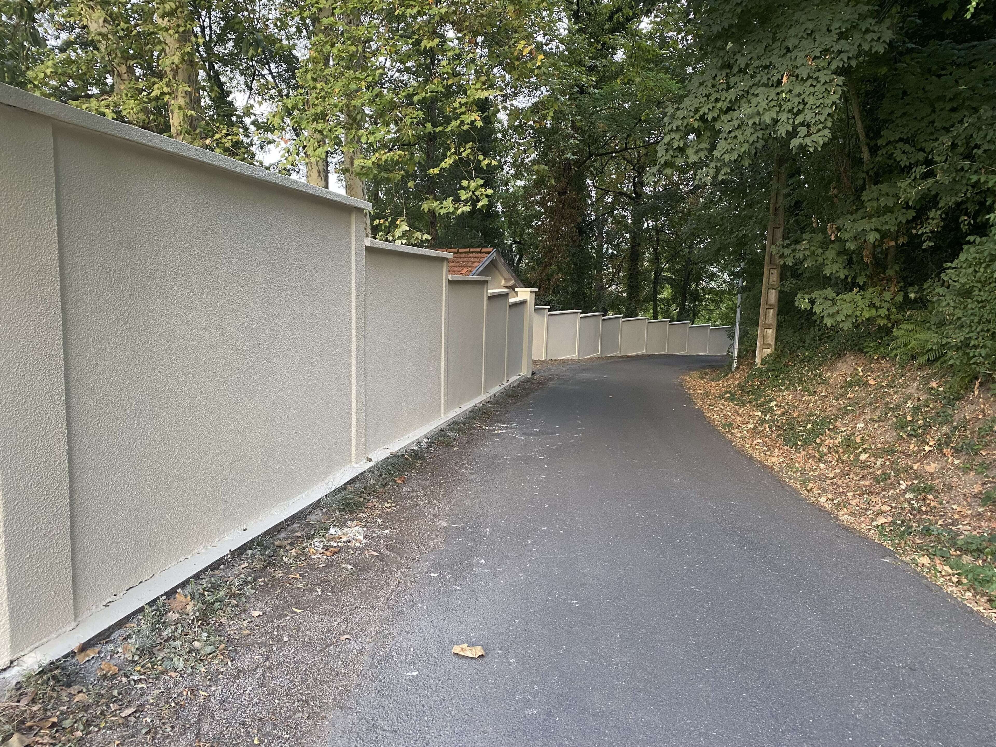 Un chemin pavé, bordé d’un petit muret en béton, et entouré d’arbres et de feuillage.