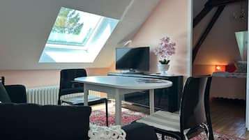 A cozy room with a skylight, a TV, a small table, and a bed.