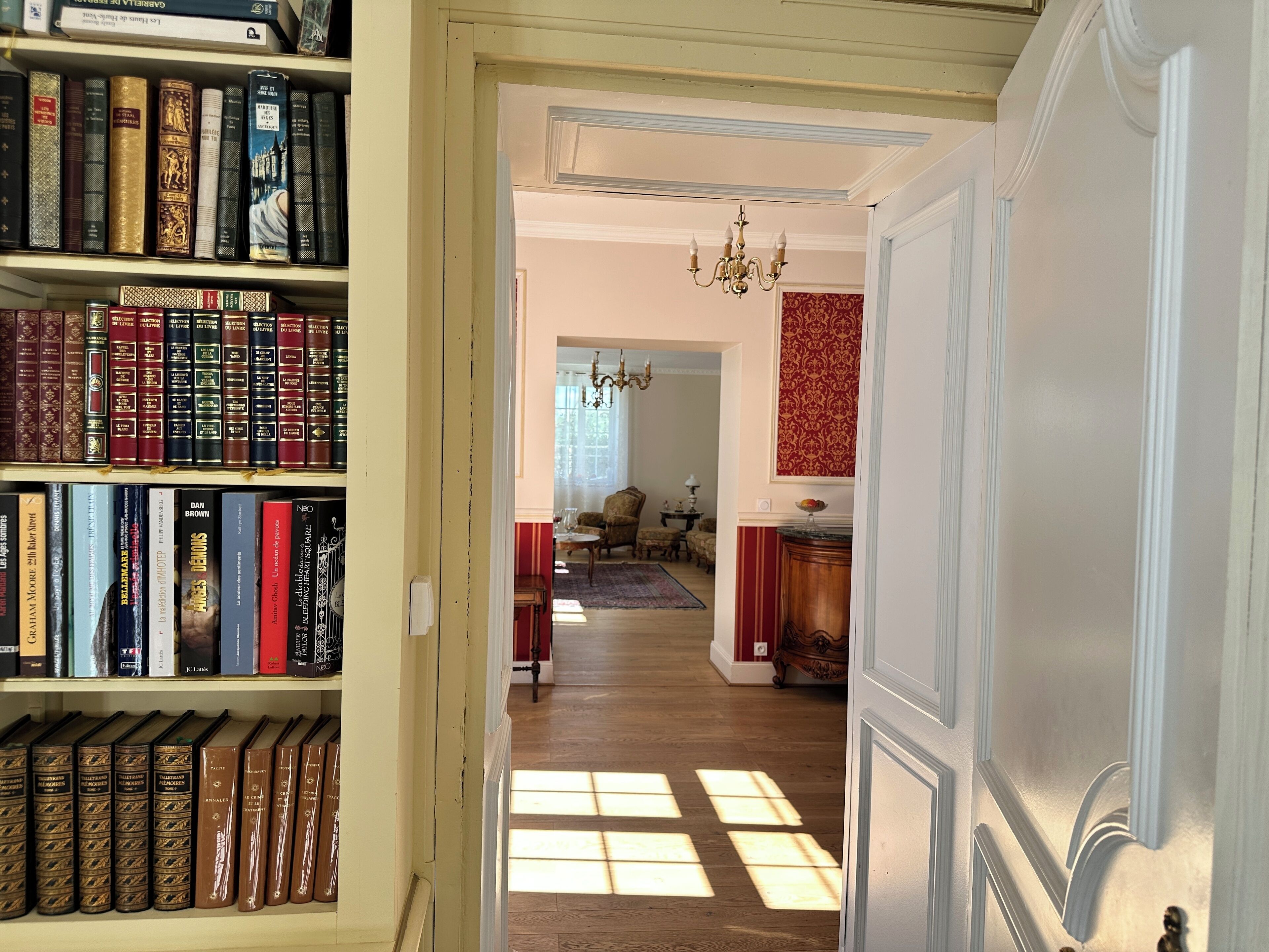 Un pasillo con estanterías a la izquierda y una habitación con candelabro a la derecha.
