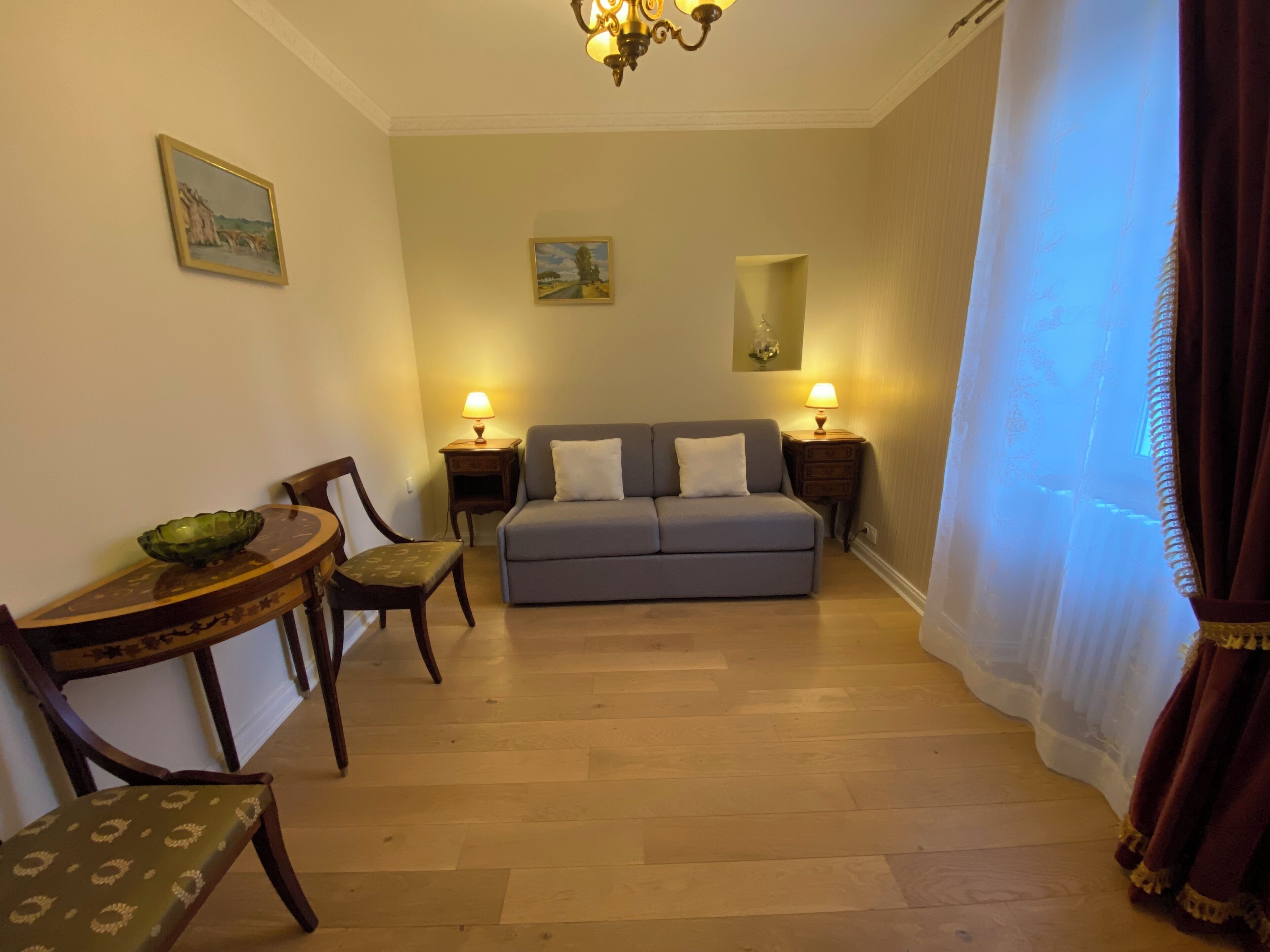 Een woonkamer met een bank, twee lampen, een eettafel met stoelen en een schilderij aan de muur.