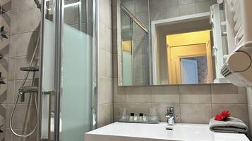 Un baño moderno con ducha envuelta en vidrio, un lavamanos blanco con un espejo encima y una toalla con un diseño floral en la encimera.
