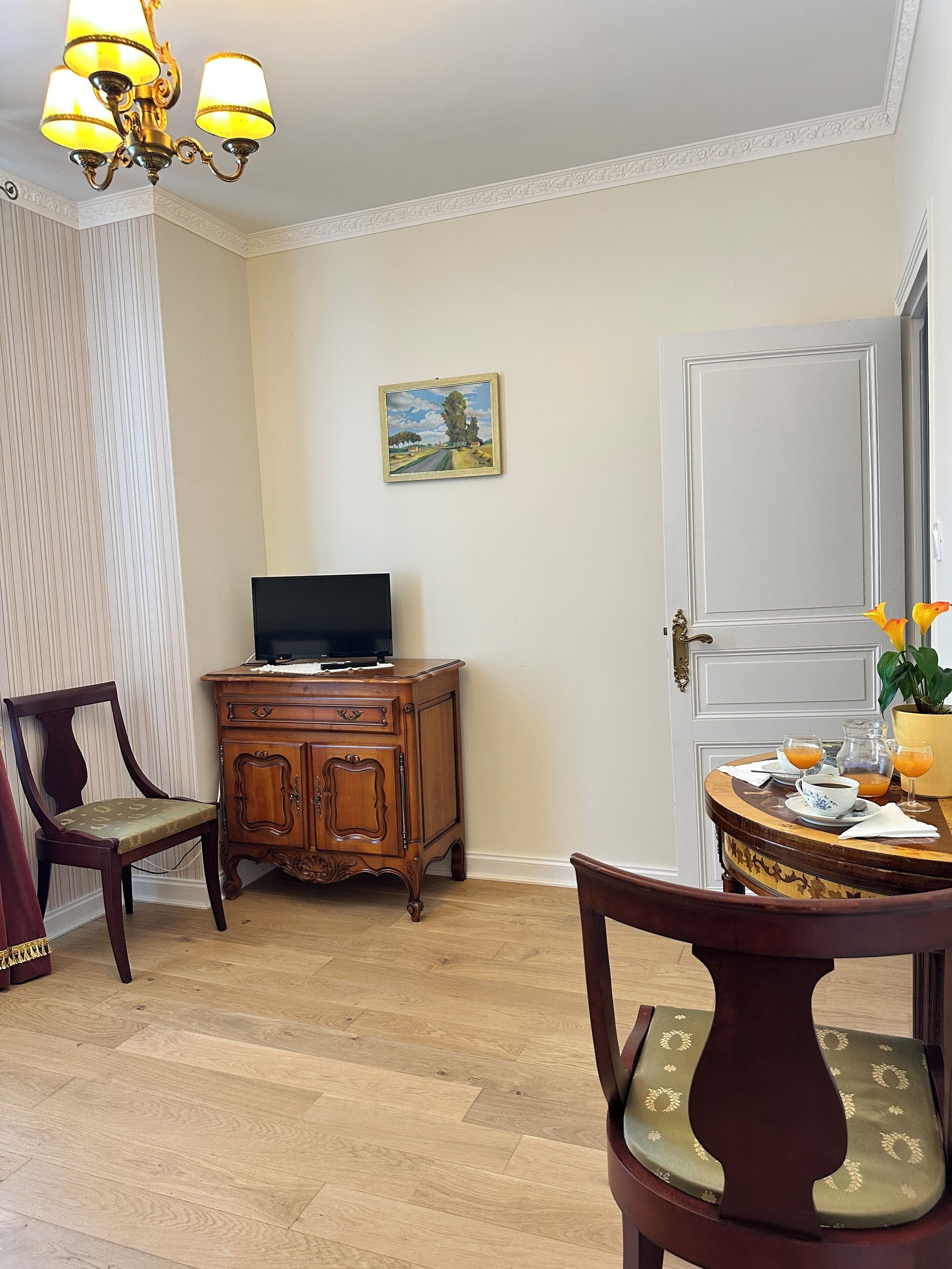 A dining area with a wooden table set for two, a television on a cabinet, and a painting on the wall.