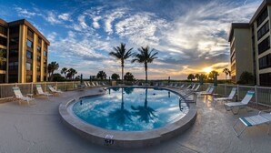 Ein kreisförmiger Pool mit Liegestühlen und Palmen, umgeben von Gebäuden.