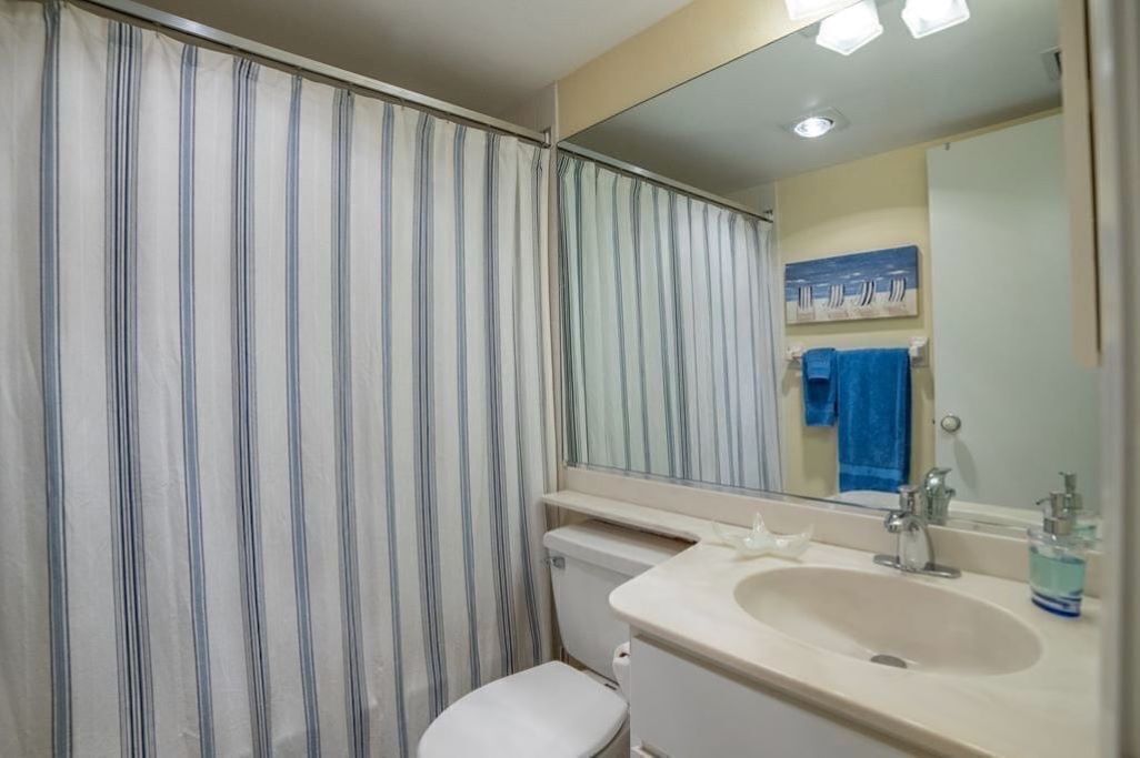 A bathroom with a striped shower curtain, a toilet, a sink with a mirror, and a blue towel hanging on the wall.