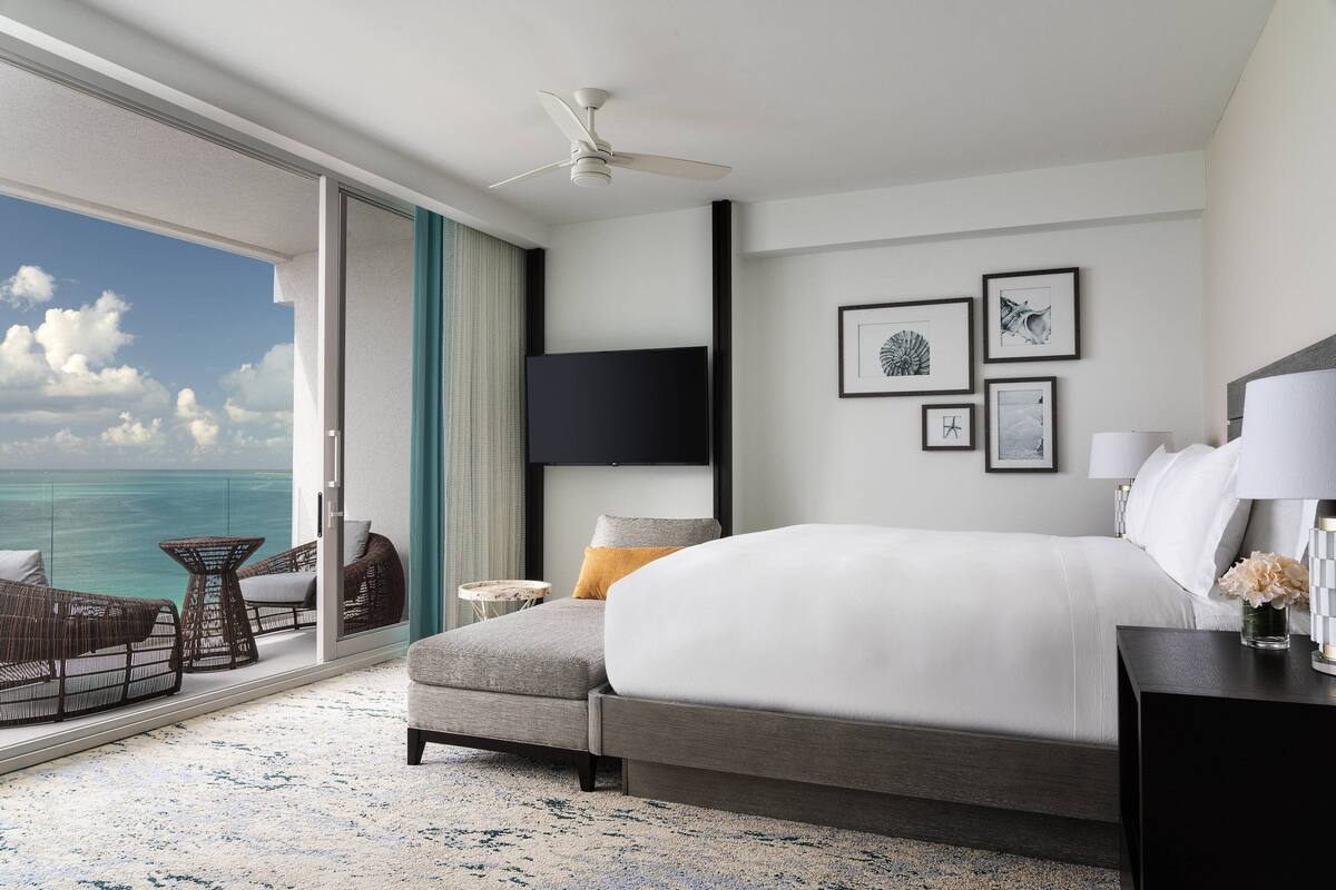 Ein modernes Hotelzimmer mit einem großen Bett, einem Deckenventilator, einem Flachbildfernseher und einem Balkon mit Blick auf den Ozean.