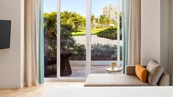 A modern living room with a sofa, a small round table, and a large sliding glass door leading to a balcony with a view of greenery and a building.