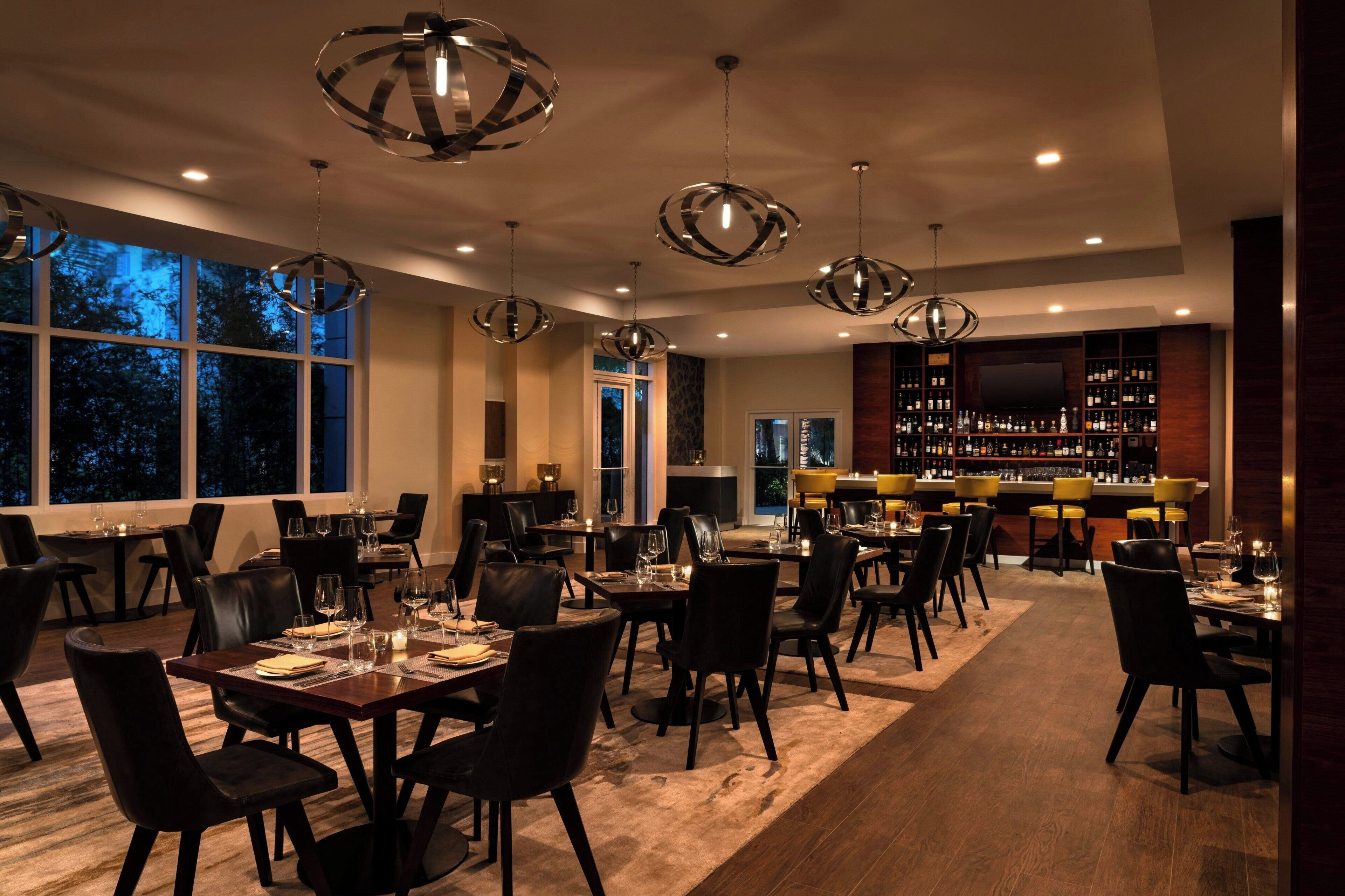 A restaurant with multiple dining tables, black chairs, and hanging spherical light fixtures.