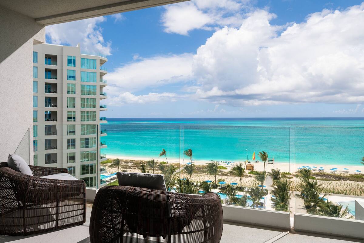 Ein Balkon mit Korbmöbeln, der Blick auf einen Strand und ein Hotelgebäude freigibt.