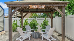 Eine hölzerne Tiki-Bar-Konstruktion mit zwei Adirondack-Stühlen und einem runden Tisch.