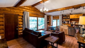 A log cabin interior with a wooden dining area, a sofa, and a kitchen with wooden cabinets and a sink.