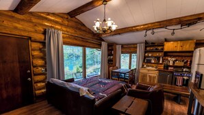 A log cabin interior with a large bed, a dining area, and a kitchen.