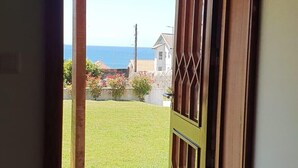 A doorway leading to a grassy area with a view of the ocean and houses in the distance.