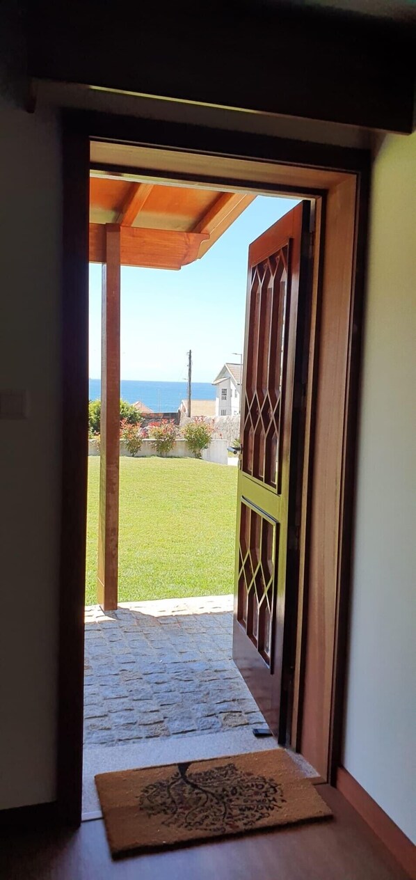 A doorway leading to a grassy area with a view of the ocean and houses in the distance. - Casa Por do Sol (Vila Nova de Gaia)