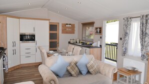 A cozy living room with a sofa and a dining table, a kitchen with white cabinets, and a view of the outside. - Herdwick Lodge. Percy Woods (Morpeth)