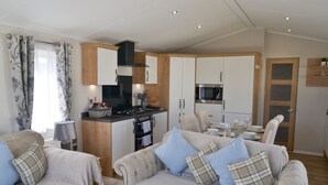 A modern living room with a sofa set, a kitchen area with cabinets and appliances, and a dining area with a table set for four. - Herdwick Lodge. Percy Woods (Morpeth)