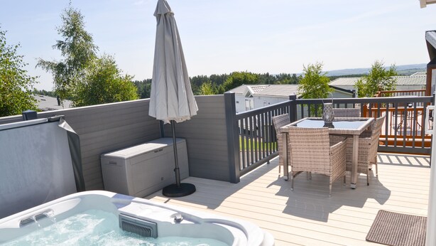 A hot tub on a wooden deck with a table and chairs, surrounded by a fence and greenery. - Herdwick Lodge. Percy Woods (Morpeth)