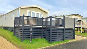 A mobile home with a fenced deck, a small porch, and a satellite dish. - Herdwick Lodge. Percy Woods (Morpeth)