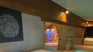 A hot tub with blue LED lights, a stone wall, and a wooden ceiling. - Charming cottage "La Caussenarde (Saint-Beauzély)