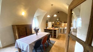 A dining area with a table set for four, a kitchen in the background, and a wooden door with a glass panel. - Charming cottage "La Caussenarde (Saint-Beauzély)