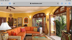 A spacious living room with a large orange sofa, a woven chair, and a coffee table. There is a large window with a view of greenery outside. - Great ocean views, walking distance to town/ beach, heated pool, family friendly (Sayulita)