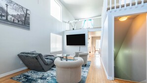 Een moderne woonkamer met een grijze bank, een beige fauteuil, een flatscreen televisie en een groot raam.