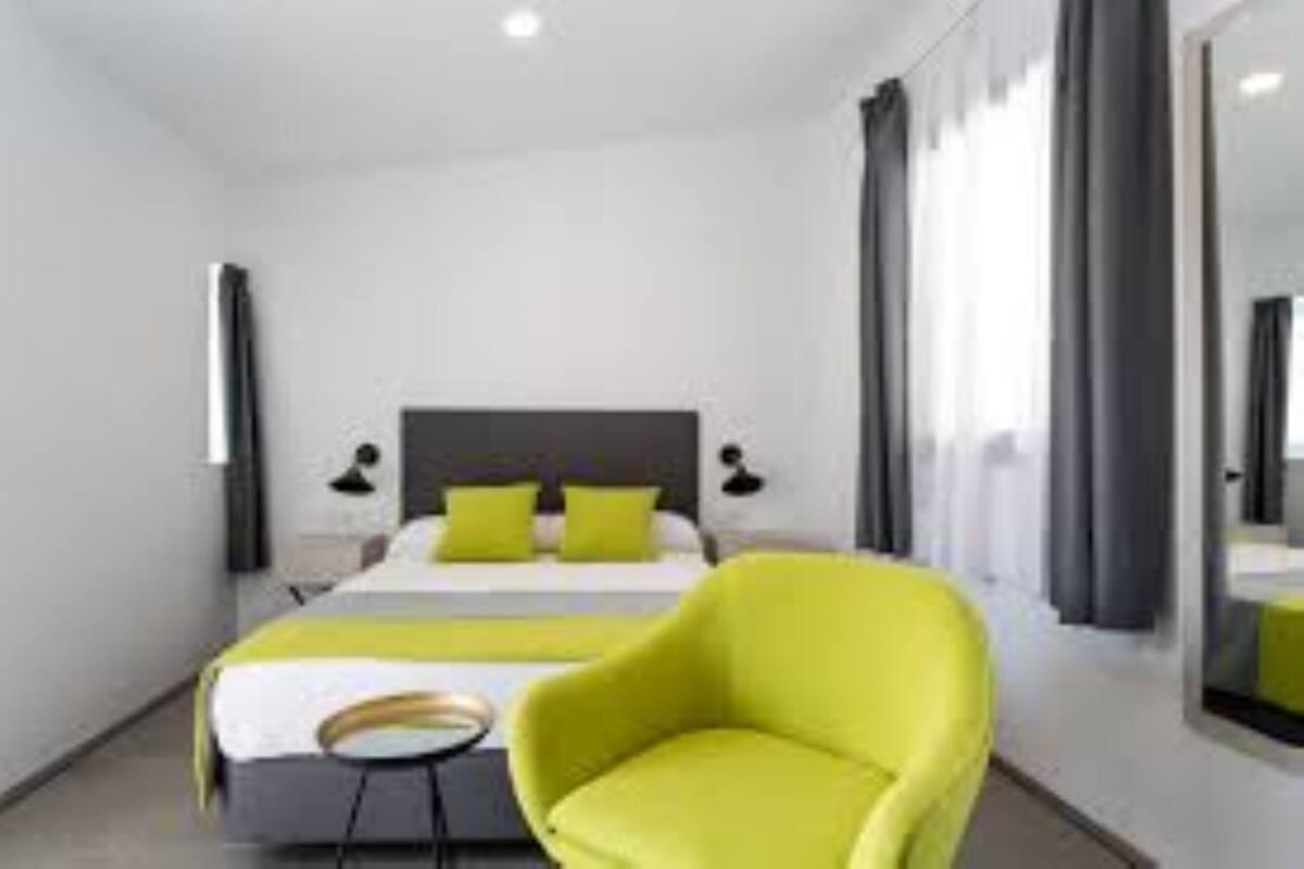 A modern hotel room with a bed, a bright yellow armchair, and a large mirror.