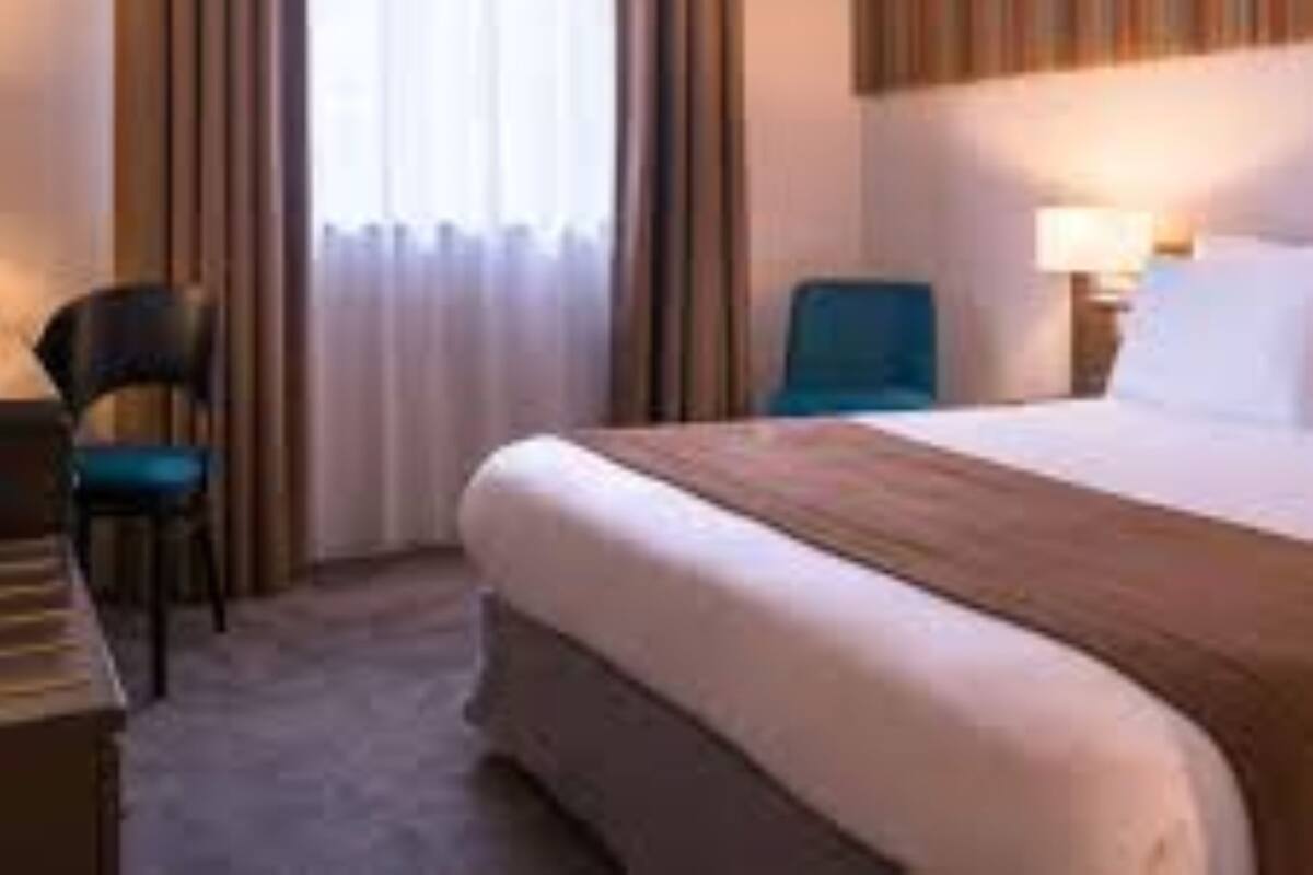 A hotel room with a bed, a desk, a chair, and a window with curtains.