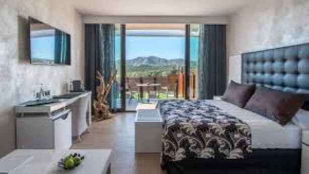 Habitació d'hotel moderna amb un llit gran, una taula de treball i vistes a les muntanyes des del balcó.