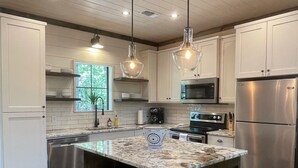 A modern kitchen with white cabinets, a central island with stools, stainless steel appliances, and pendant lighting.