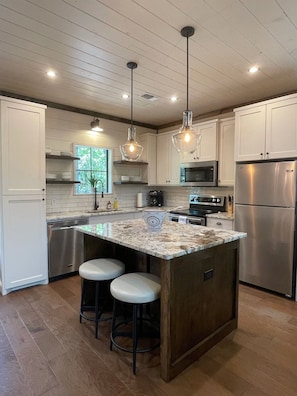 A modern kitchen with white cabinets, a central island with stools, stainless steel appliances, and pendant lighting.