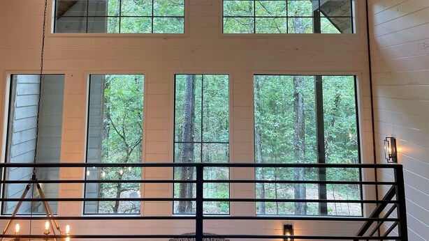 A cabin with a high ceiling, multiple windows, a chandelier, and a welcome sign.