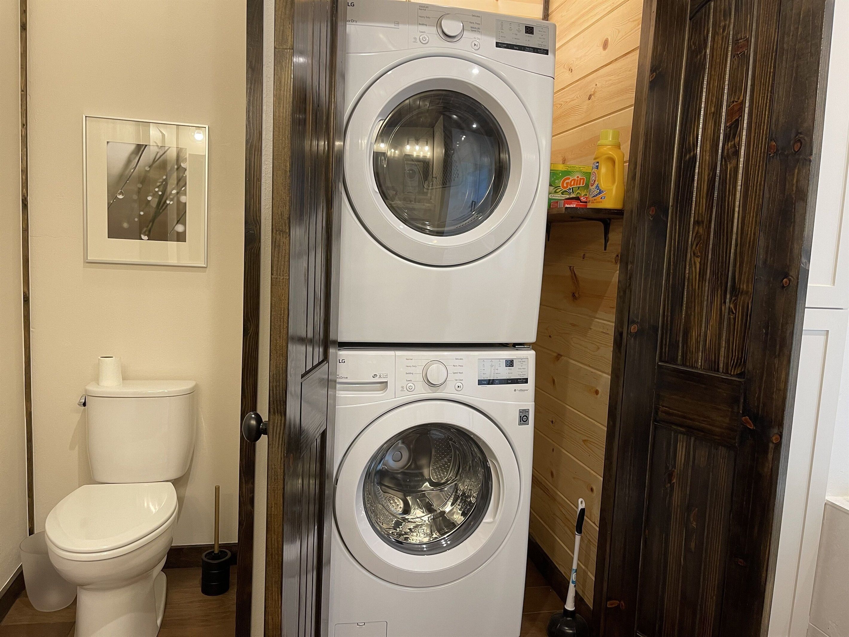 Una lavanderia con due lavatrici affiancate, un water e una porta in legno.