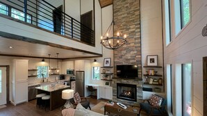 A spacious living area with a fireplace, a kitchen with modern appliances, and a high ceiling with exposed beams.