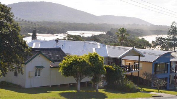 A residential area with houses featuring solar panels, surrounded by greenery and hills in the background.