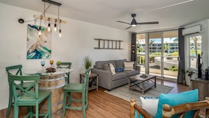 A modern living room with a dining area, a grey sofa, and a ceiling fan. - Maui Banyan G410 - Remodeled, Partial Ocean View, AC, Across Kamaole Beach! (Kihei)