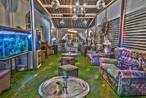 Un espacio interior con suelo de césped artificial verde, diversas opciones de asientos como sofás y sillones, un acuario grande e iluminación decorativa.