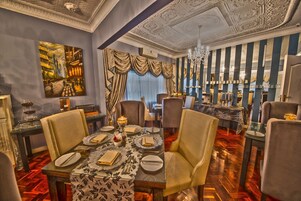 A luxurious dining room with ornate ceiling, elegant chairs, and a table set for a meal.