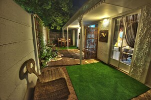 A covered outdoor area with artificial grass, wicker furniture, and a wooden pergola.