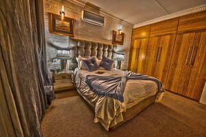 A bedroom with a large bed, a wooden wardrobe, and a wall-mounted air conditioning unit.