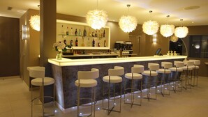 A modern bar area with a long counter and multiple stools, a well-stocked bar with various bottles, and decorative spherical lights. - Oz Apos Inn Hotel (Agde)