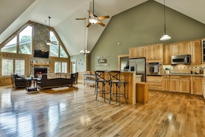 A spacious kitchen with wooden cabinets, a large island with bar stools, and a stone fireplace. - All Decked Out w/ Hot tub 4 BR+Loft, Game Room (Ellijay)