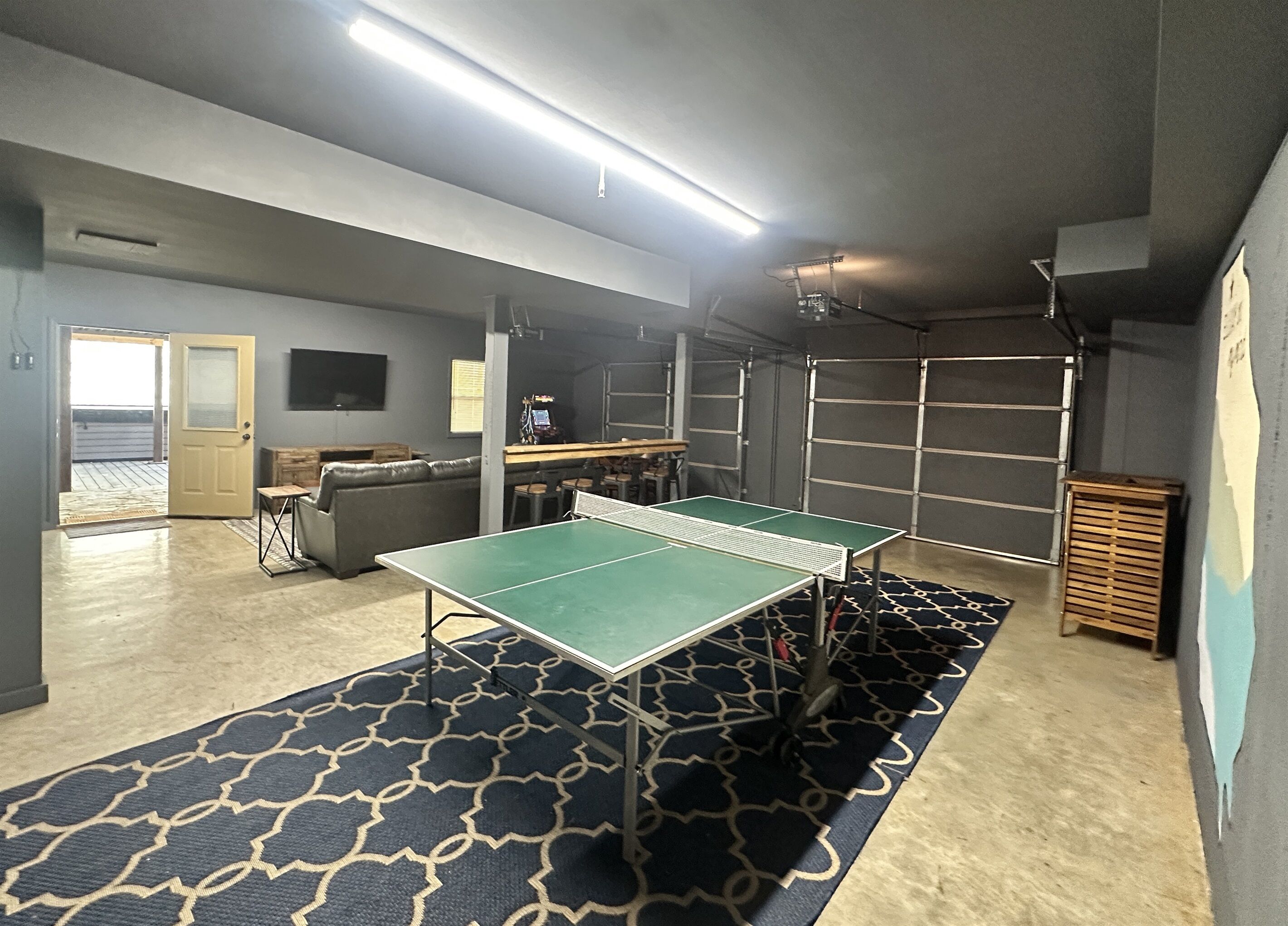 Et værelse med et ping pong bord, en sofa og et barområde med barstole.