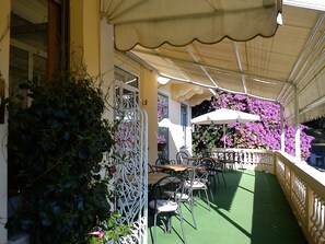 An outdoor café with tables and chairs, covered by a canopy, and surrounded by greenery and flowers. - Canali (Rapallo)