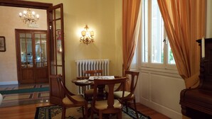 A dining area with a round table, four chairs, a chandelier, and a window with curtains. - Canali (Rapallo)