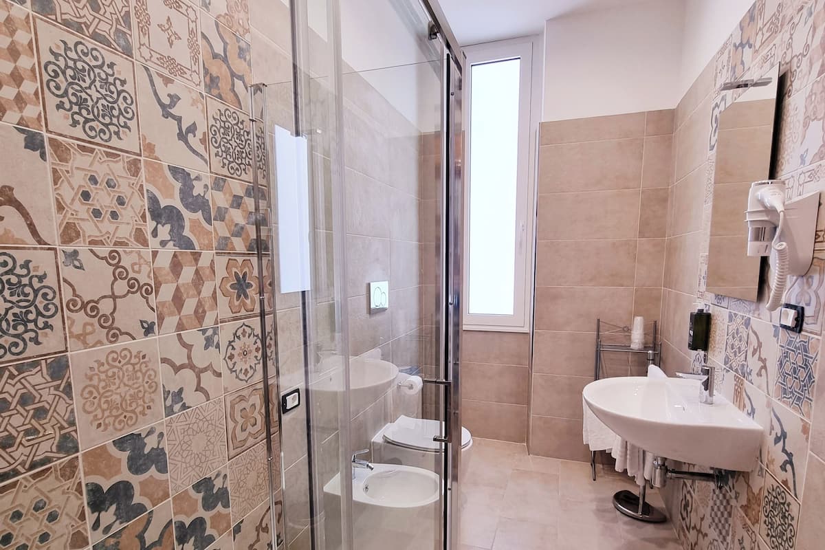 A modern bathroom with patterned tiles, a glass shower enclosure, a toilet, a sink, and a mirror.